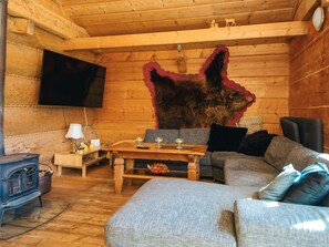A cozy cabin interior with a wooden interior, a mounted television, a dining table with glasses, and a large fur rug.