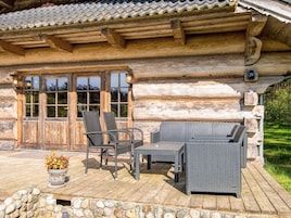 A log cabin with a porch, outdoor seating, and a stone wall.