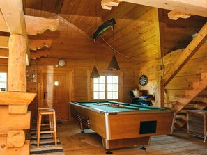 Un interior de madera con una mesa de billar, un dardo y una escalera.