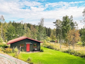 A small, dark green wooden cabin with a red roof and two windows, surrounded by a well-maintained lawn and dense forest. - 3 Person Holiday Home in Henan (Henån)