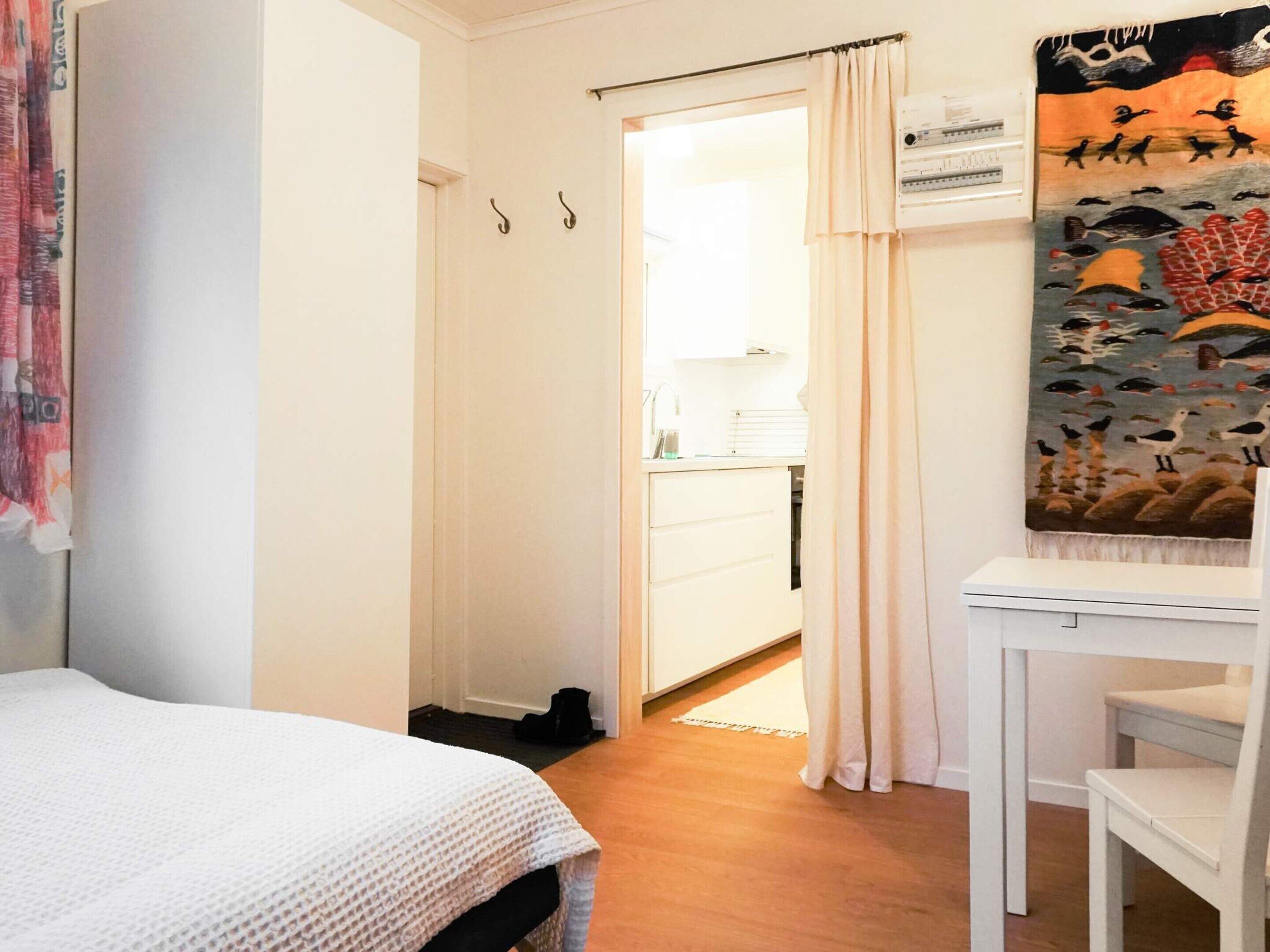 A bedroom with a bed, a desk, and a chair. There is a door leading to a bathroom with a sink and a towel rack.