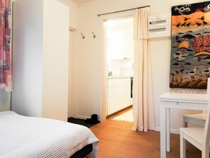 A bedroom with a bed, a desk, and a chair. There is a door leading to a bathroom with a sink and a towel rack.