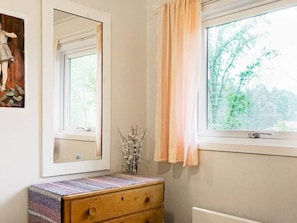A bathroom with a wooden dresser, a mirror, a window with a view of trees, and a vase with branches. - 3 Person Holiday Home in Henan (Henån)