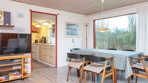 Una stanza accogliente con pavimento in legno, un tavolo da pranzo con sedie, una TV su un mobile e una zona cucina visibile attraverso una porta aperta.