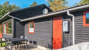 Una baita di legno con una vasca idromassaggio, un tavolo con sedie e una finestra con una porta rossa.