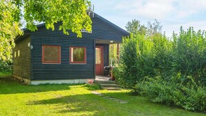 Una baita di legno scuro con una porta rossa, un piccolo portico e un giardino curato.