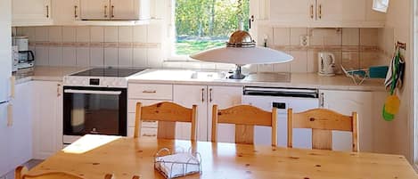 A kitchen with white cabinets, a stove, a sink, and a dining table with chairs.