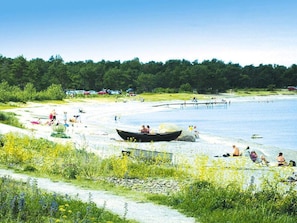 A beach with a boat, people sunbathing, and a forest in the background.