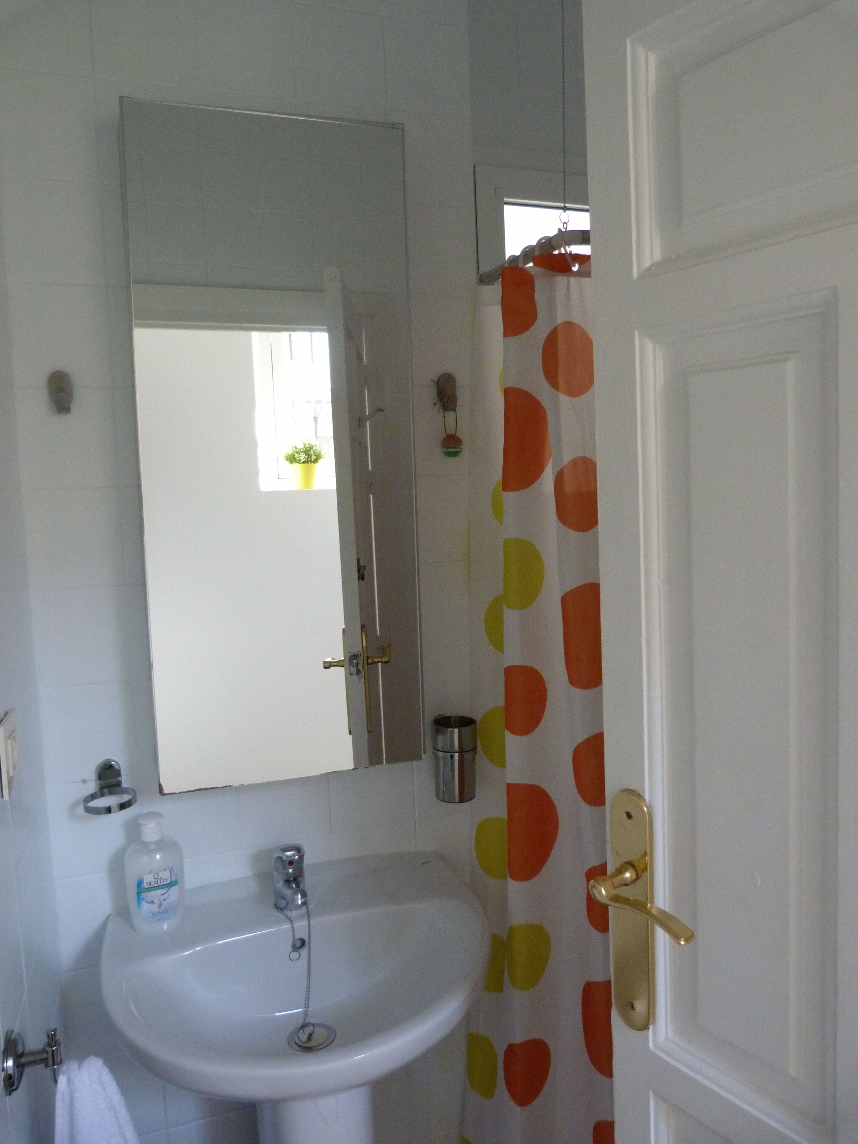 Une salle de bain avec un lavabo blanc, un miroir et un rideau de douche orné de pois orange et jaunes.
