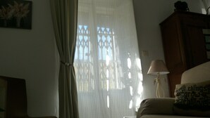 A room with a bed, a lamp, a small table, and a window with curtains. - Charming, very bright historic center (Sevilla)
