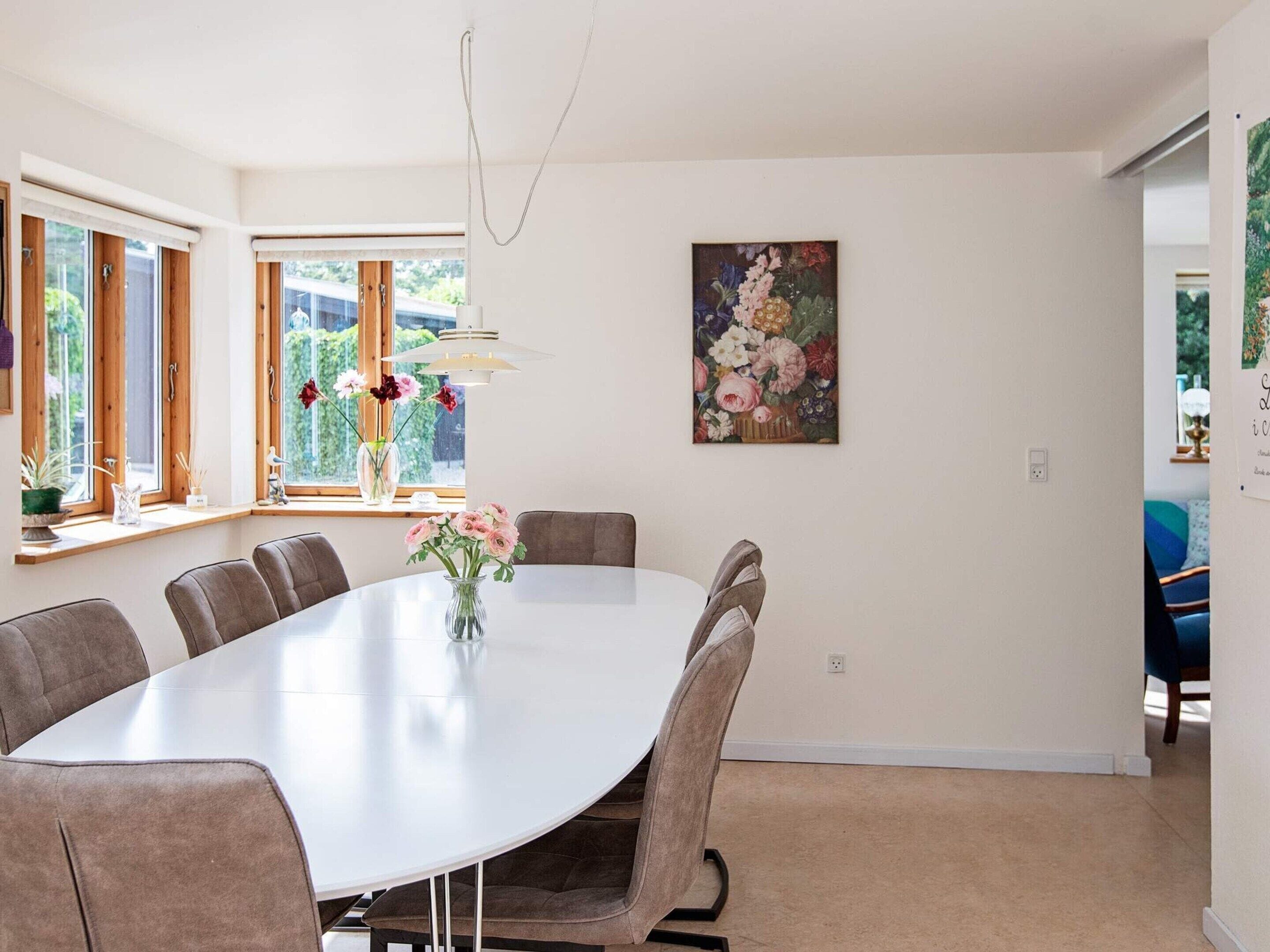 A dining area with a round table, chairs, a vase of flowers, and a painting on the wall.