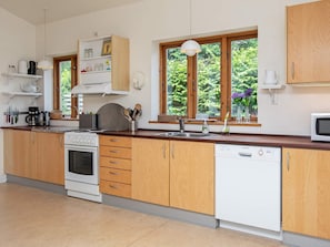 A kitchen with wooden cabinets, a stove, a dishwasher, and a window with a view of greenery.