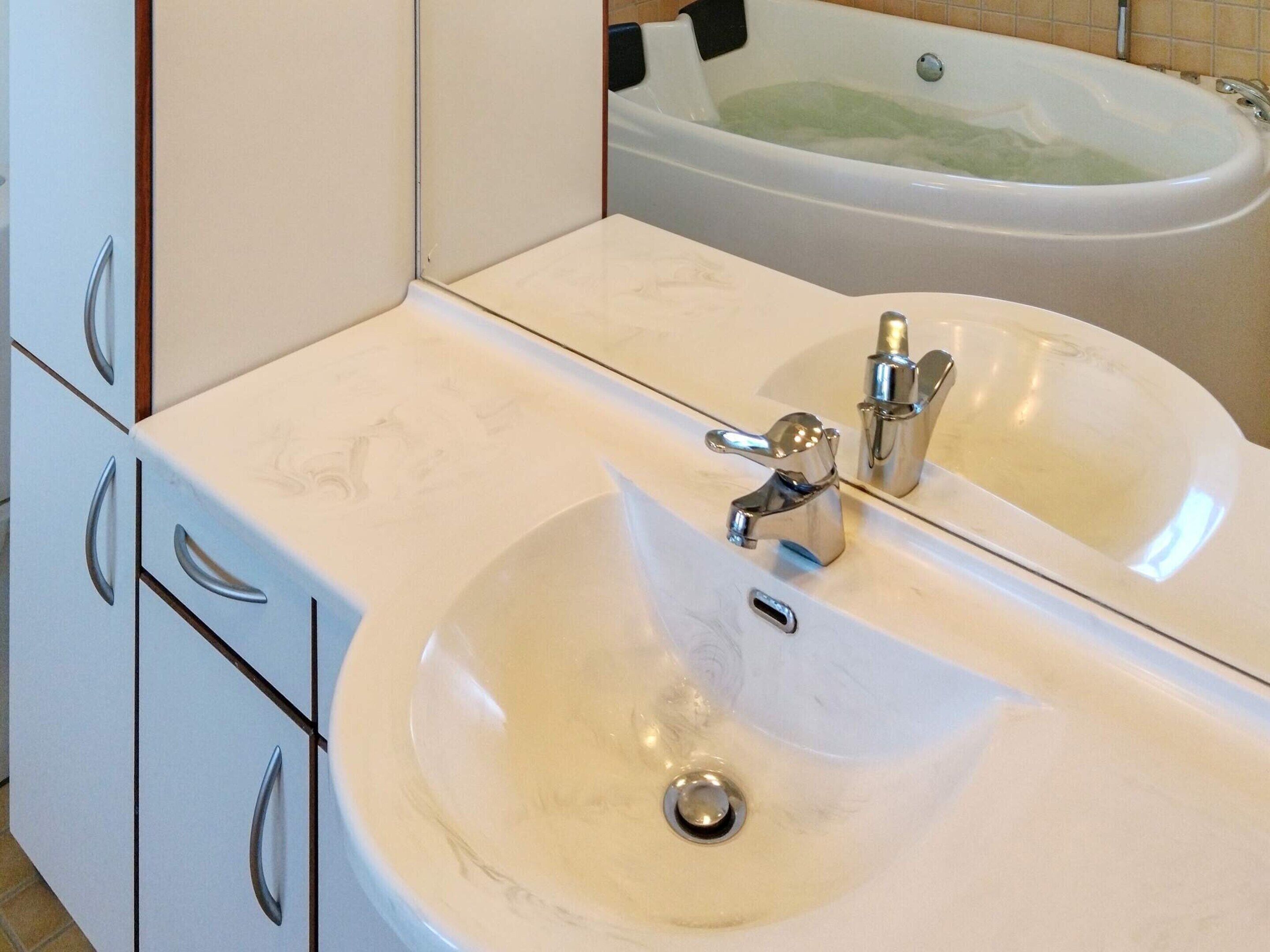 Un baño con lavamanos blanco, espejo y bañera.