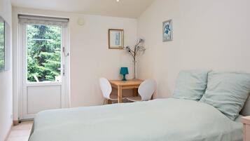 A bedroom with a bed, a desk, two chairs, a window, and a door.