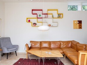 A living room with a brown leather sofa, a wooden coffee table, a gray armchair, and a red patterned rug.