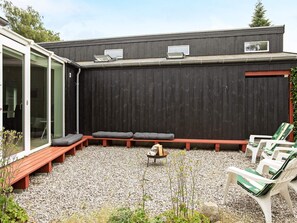 A covered outdoor seating area with benches and chairs, a fire pit, and a gravel ground.