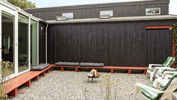 A covered outdoor seating area with benches and chairs, a fire pit, and a gravel ground.