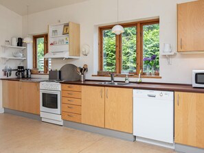 A kitchen with wooden cabinets, a stove, a dishwasher, and a window with a view of greenery.