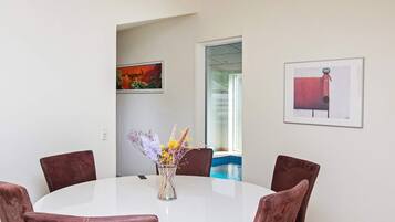 A round dining table with six chairs, a vase with flowers, and two framed artworks on the wall.