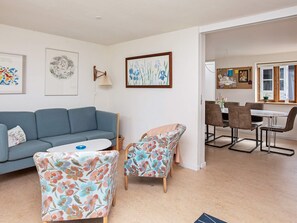 A living room with a blue sofa, floral armchairs, a round coffee table, and a dining area with a table and chairs.