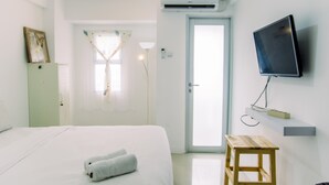 A hotel room with a bed, a TV mounted on the wall, a wooden stool, and a door leading to the outside. - Elegant And Comfortable Studio At Urbantown Serpong Apartment (South Tangerang)
