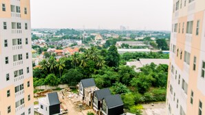 A high-rise building with multiple balconies and a view of a residential area with houses and greenery. - Elegant And Comfortable Studio At Urbantown Serpong Apartment (South Tangerang)