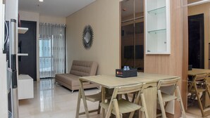A modern living room with a beige sofa, a glass-top dining table with wooden chairs, a mirror, and a black box on the table. - Exclusive And Comfort 2Br Apartment At Sudirman Suites (Jakarta)