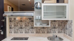 A modern kitchen with a stainless steel range hood, a built-in glass shelf with dishes, a sink, and a patterned tile backsplash. - Exclusive And Comfort 2Br Apartment At Sudirman Suites (Jakarta)