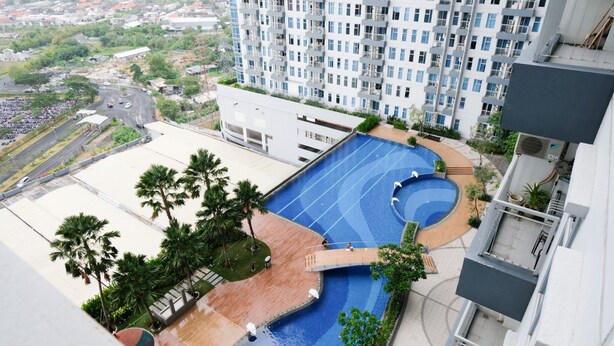 Edifício residencial com piscina no terraço, cercado por vegetação e vista para a cidade.