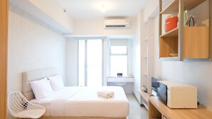 Quarto de hotel moderno com cama, poltrona, escrivaninha e computador, e televisão.