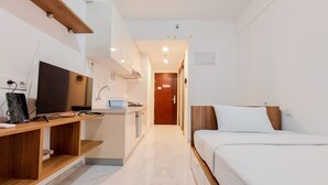 A hotel room with a bed, a desk with a computer, a TV, and a kitchenette. - Homey And Warm Studio Room At Sky House Bsd Apartment (Pagedangan)