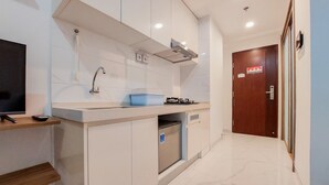 A modern kitchen with white cabinets, a built-in stove, and a sink. - Homey And Warm Studio Room At Sky House Bsd Apartment (Pagedangan)
