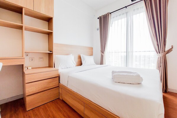 Une chambre d’hôtel bien rangée, avec un lit, un meuble de rangement en bois et une fenêtre avec des rideaux.