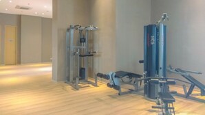 Un gimnasio con diversas máquinas de ejercicio, un banco y una puerta al fondo.