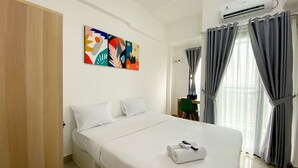 A hotel room with a bed, a painting on the wall, and an air conditioning unit.
