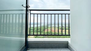 A balcony with a metal railing, a view of a green landscape, and a cloudy sky.