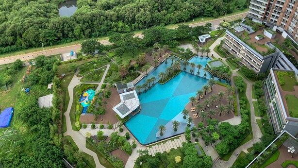 Ein großer Swimmingpool, umgeben von Palmen und viel Grün, mit Blick auf einen Fluss und eine Brücke im Hintergrund.