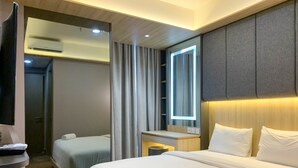 Ein Hotelzimmer mit einem großen Bett, einem kleineren Bett, einem Schreibtisch, einem Spiegel und einer Klimaanlage.