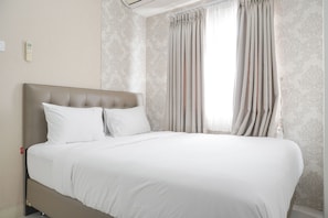 A neatly made bed with white linens in a room with patterned wallpaper and a large window with curtains. - Cozy And Well Designed 2Br At Green Pramuka City Apartment (Jakarta)