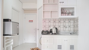A modern kitchen with white cabinetry, a stainless steel refrigerator, a coffee maker, and a tiled backsplash. - Cozy And Well Designed 2Br At Green Pramuka City Apartment (Jakarta)