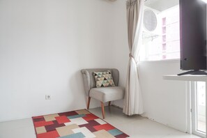 Une pièce comprenant une chaise, un tapis à motifs, un téléviseur et une fenêtre avec des rideaux.