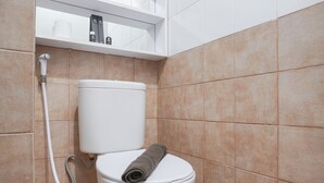 A bathroom with a toilet, a showerhead, and a shelf with toiletries. - Cozy And Well Designed 2Br At Green Pramuka City Apartment (Jakarta)
