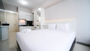 A hotel room with a neatly made bed, a small kitchenette, and a bathroom with a mirror. - Nice And Comfy Studio At Supermall Mansion Apartment (Surabaya)