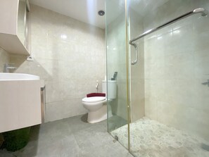 Baño con cabina de ducha de vidrio, inodoro y lavamanos.