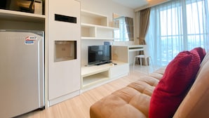 Een moderne hotelkamer met een flatscreen televisie, een koelkast, een zithoek en een groot raam met gordijnen.