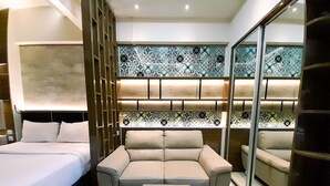 A modern hotel room with a bed, a sofa, a wooden coffee table, and a patterned wall. - Cozy Studio Room At Uttara The Icon Apartment (Depok)