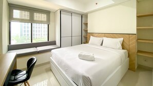 A modern bedroom with a bed, a desk, and a chair. There is a window with blinds, a wardrobe, and a shelf unit. - Cozy And Minimalist Studio At Pollux Chadstone Apartment (Cikarang)