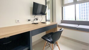 A modern office space with a desk, chair, and a large window with a view of buildings. - Cozy And Minimalist Studio At Pollux Chadstone Apartment (Cikarang)