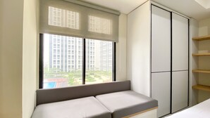 A room with a built-in bench, a wardrobe, and a window with a view of high-rise buildings. - Cozy And Minimalist Studio At Pollux Chadstone Apartment (Cikarang)