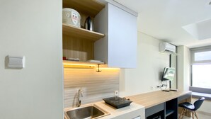 A modern kitchen with a built-in sink, a coffee maker, and a microwave on a wooden shelf. - Cozy And Minimalist Studio At Pollux Chadstone Apartment (Cikarang)